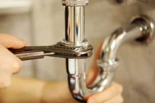 Plumber tightening a chrome pipe with a wrench under a sink