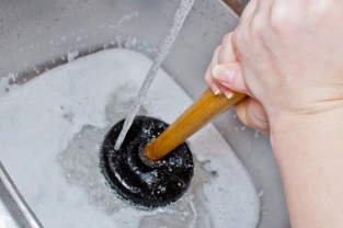 Plumber using plunger to unclog kitchen sink drain under running water